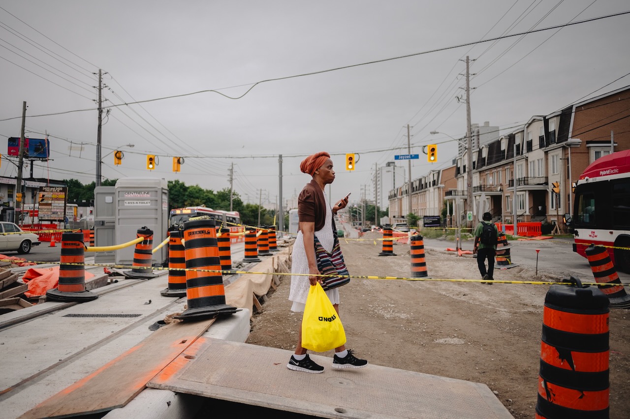 People cross the intersection at Jayzel Drive and Finch West, among construction material for the LRT corridor, in Toronto, Ont., on Thursday Aug. 24, 2023. (Christopher Katsarov Luna/cred})