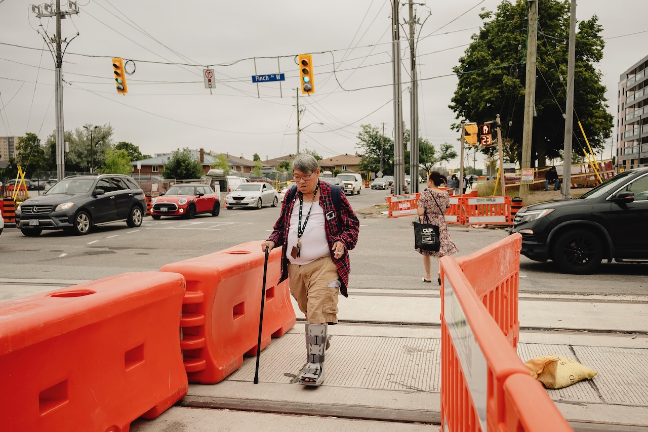 People cross within barriers at Finch West and Oakdale Rd., along the Finch West LRT corridor, in Toronto, Ont., on Thursday Aug. 24, 2023. (Christopher Katsarov Luna/cred})