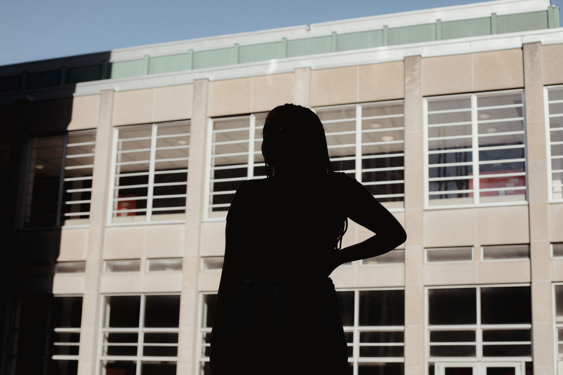 Amina, who was sexually assaulted in 2023, stands in silhouette on the University of Toronto campus. She is visible only in shadow.