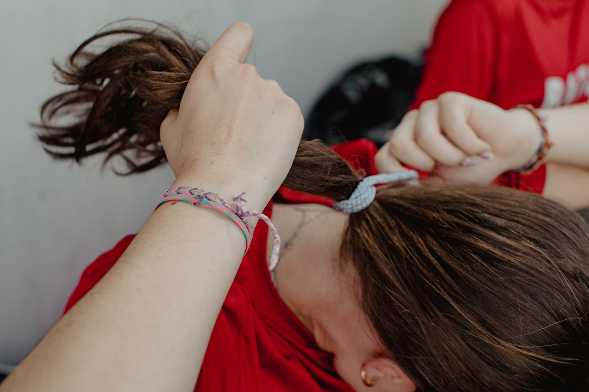 Left, an athlete looks on as her teammates play ball hockey. Right, an athlete ties back her hair before being called to play.